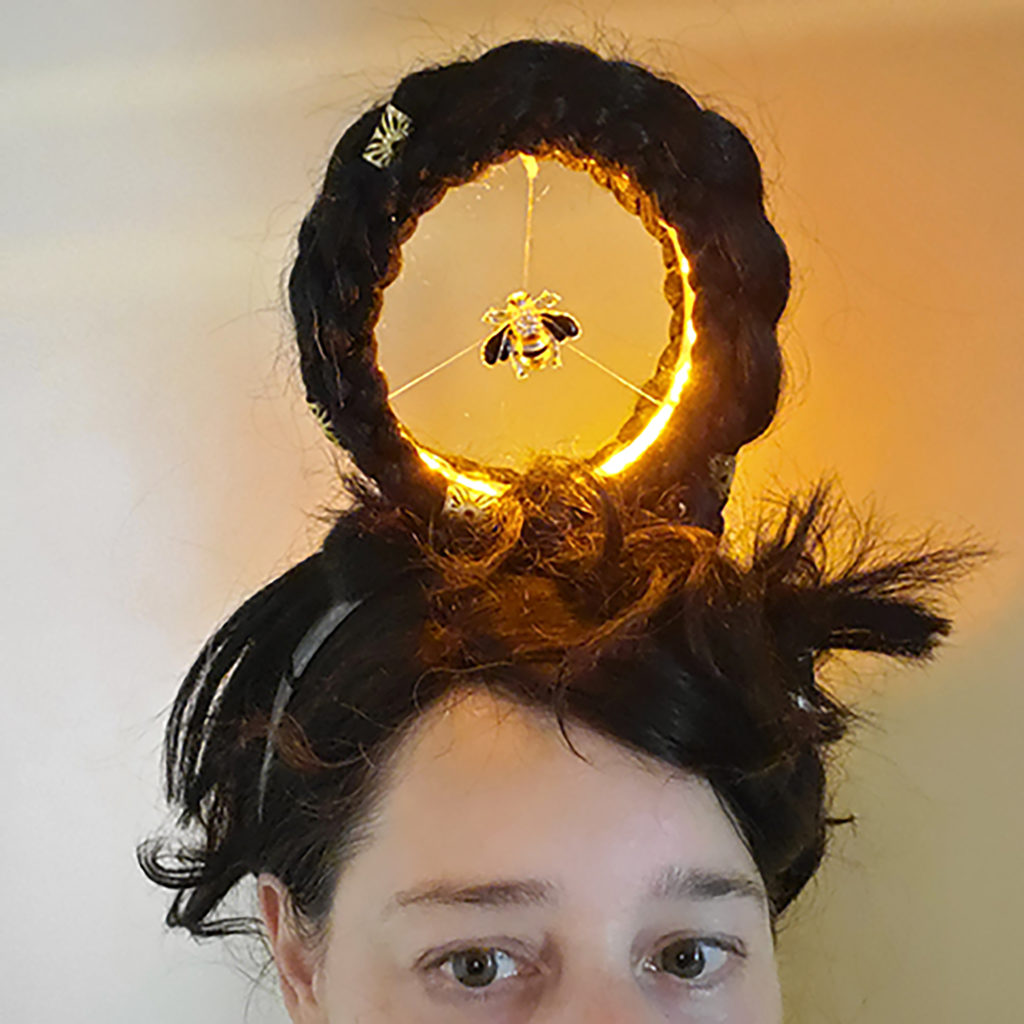 person wearing a giant hair braid hoop on top of their head. The hair hoop is lit from within and there there is a bee inside